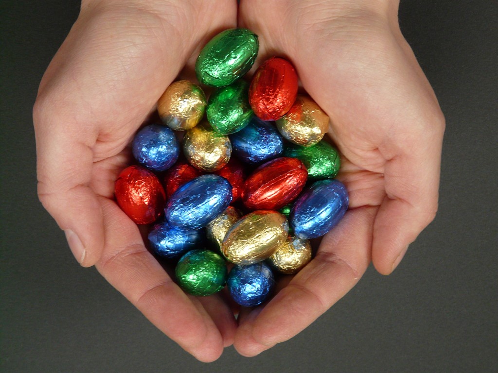Two hands cupping lots of small chocolate easter eggs in bright coloured foils
