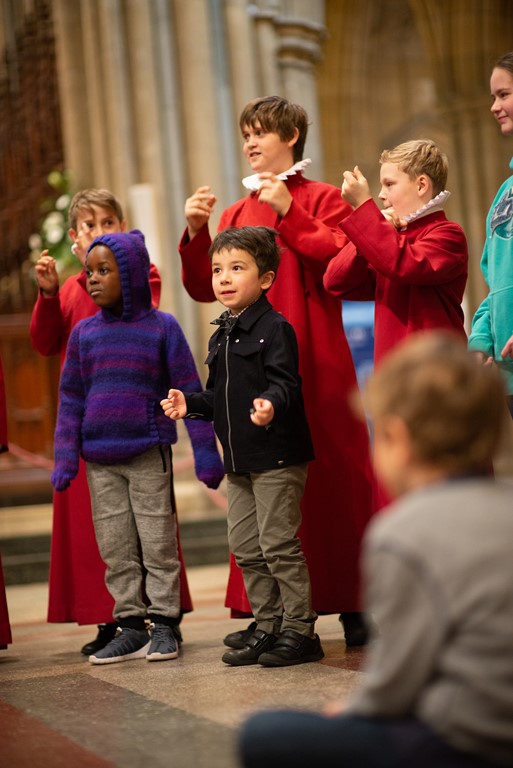 Truro Cathedral choristers in cassocks clicking their fingers with younger children joining in